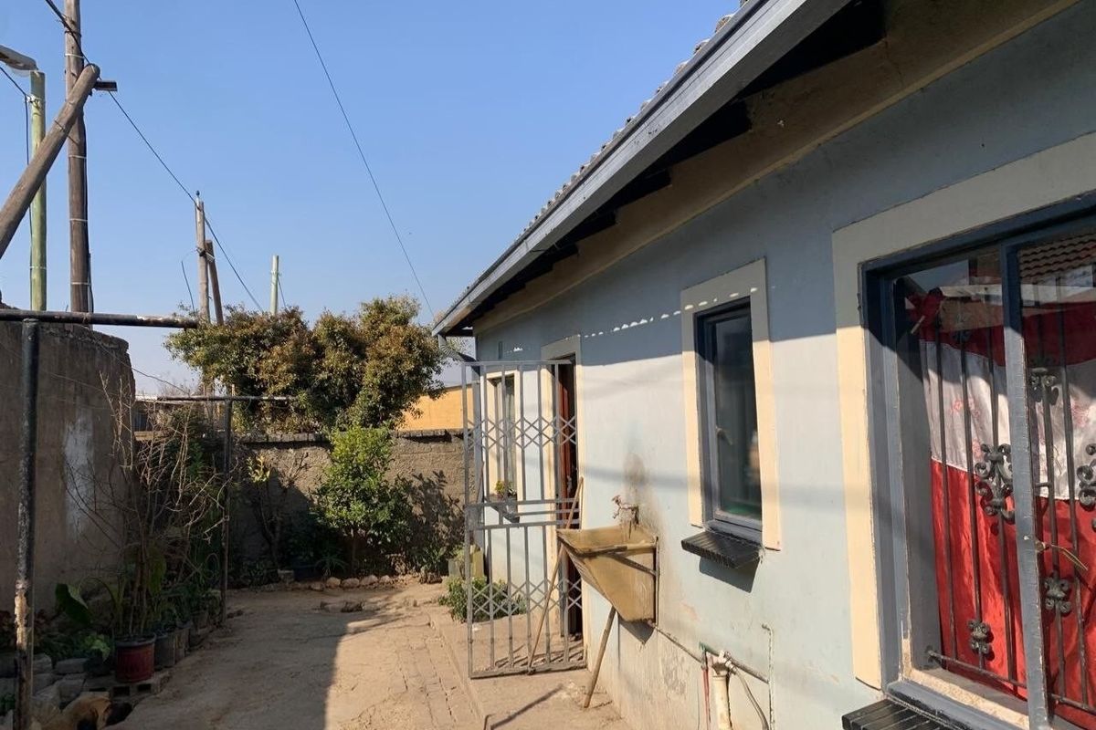 Rear exterior view of the property featuring a utility sink, security gate, and perimeter wall with visible wear to the exterior finishes.