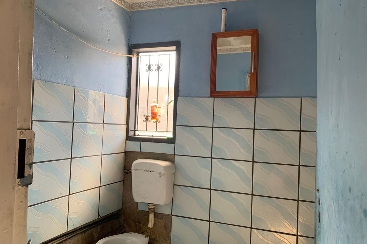 A small bathroom featuring tiled walls, a standard toilet with a high-level cistern, and a wall-mounted mirror cabinet, requiring cosmetic updates and repairs.