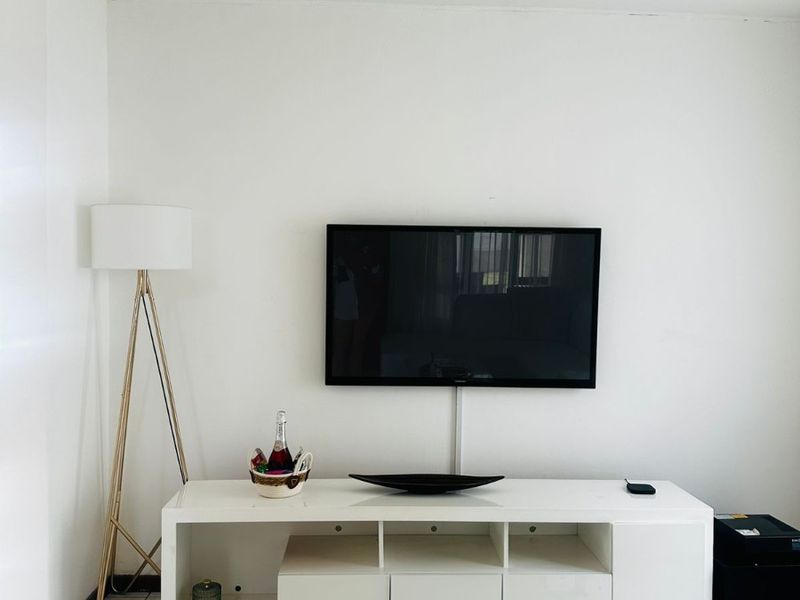 A simple living room area featuring neutral tiled flooring and a wall-mounted television setup.