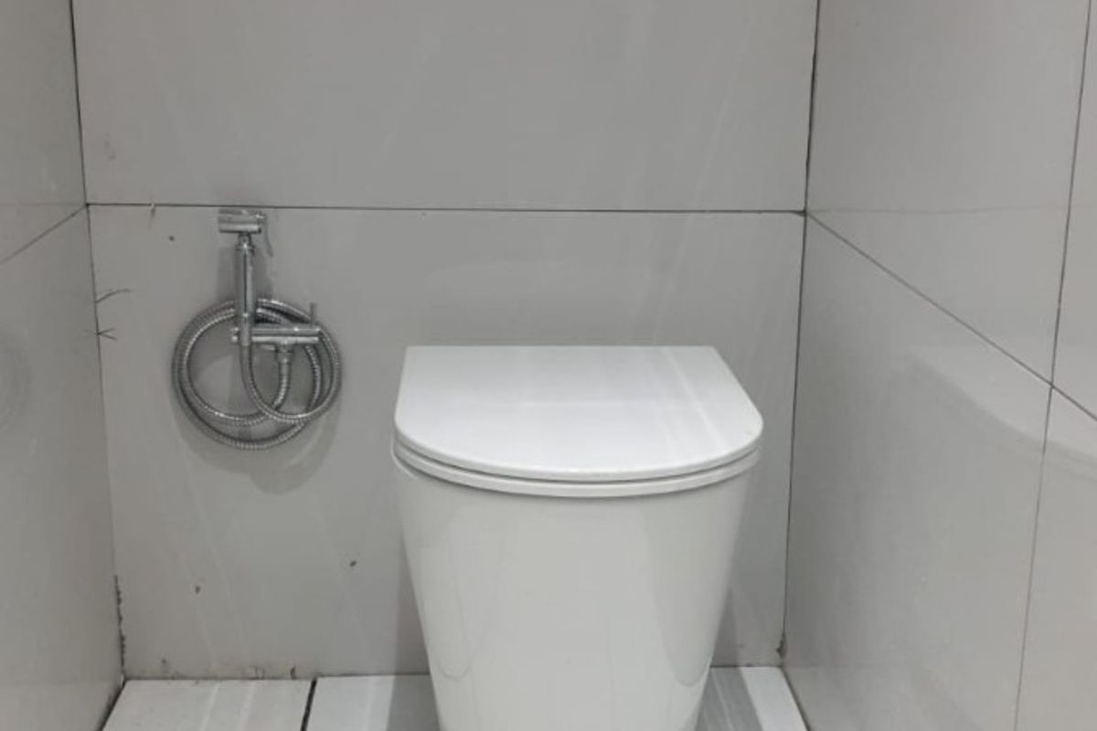 A compact bathroom featuring a modern wall-mounted toilet with a concealed cistern and bidet spray, finished with white ceramic wall and floor tiles.