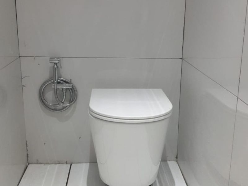 A compact bathroom featuring a modern wall-mounted toilet with a concealed cistern and bidet spray, finished with white ceramic wall and floor tiles.