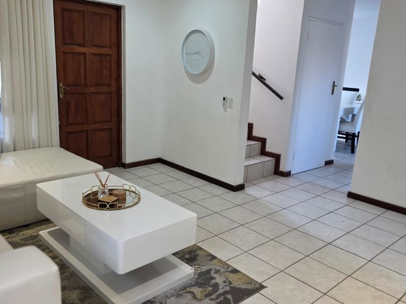 A living area featuring tiled flooring, a wooden entrance door, and a staircase leading to the upper level.