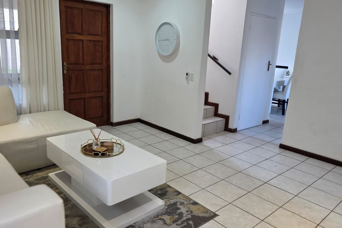 A living area featuring tiled flooring, a wooden entrance door, and a staircase leading to the upper level.