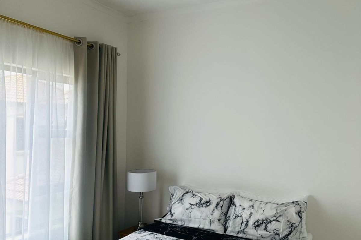 A bright bedroom featuring neutral tiled flooring, recessed downlighting, and large windows with installed curtain rods.