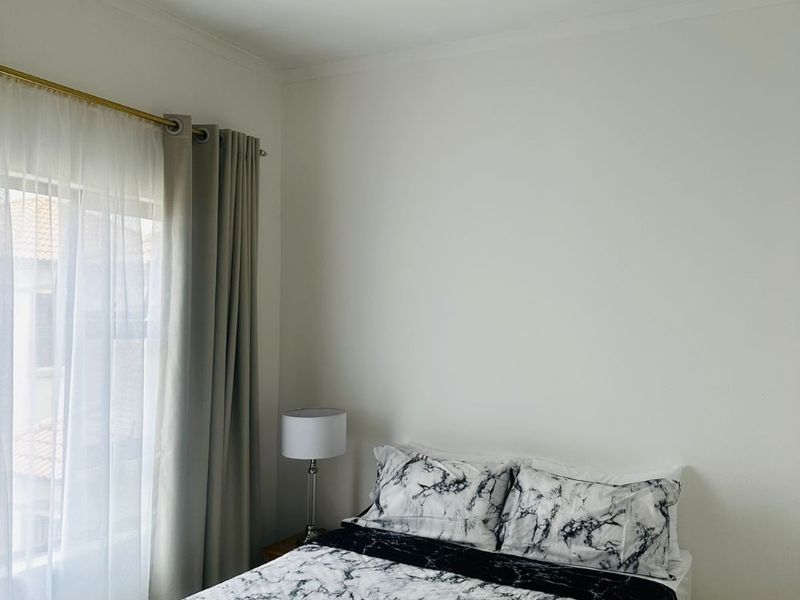 A bright bedroom featuring neutral tiled flooring, recessed downlighting, and large windows with installed curtain rods.