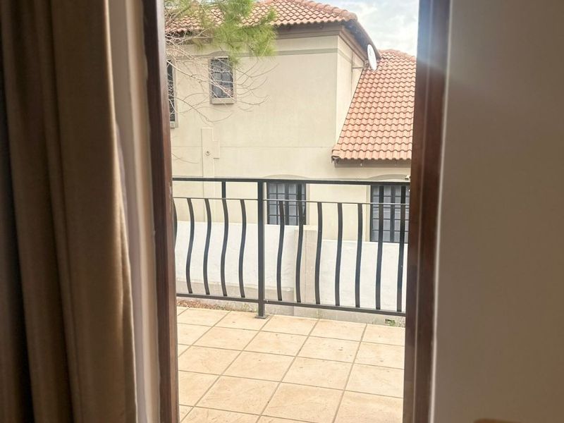 A view from an interior room looking out onto a tiled balcony with a metal balustrade and overhead awning.