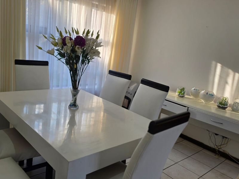 A dining room area featuring tiled flooring and natural light through window curtains.