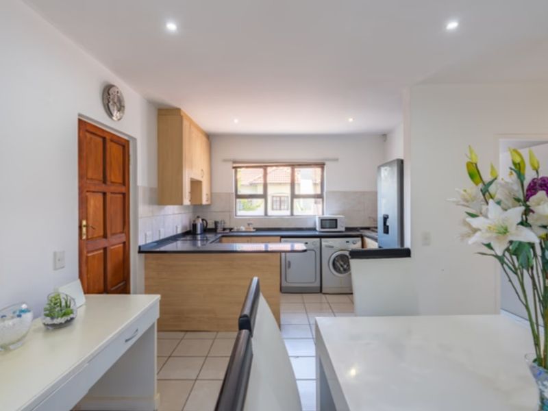 Functional kitchen featuring light wood cabinetry, dark countertops, tiled backsplash, and integrated laundry appliances, with direct access to adjacent living space.