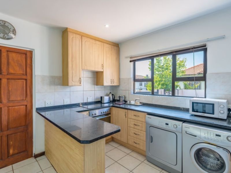 A functional kitchen featuring light wood cabinetry, dark granite countertops, tiled backsplash, and integrated laundry appliance space.