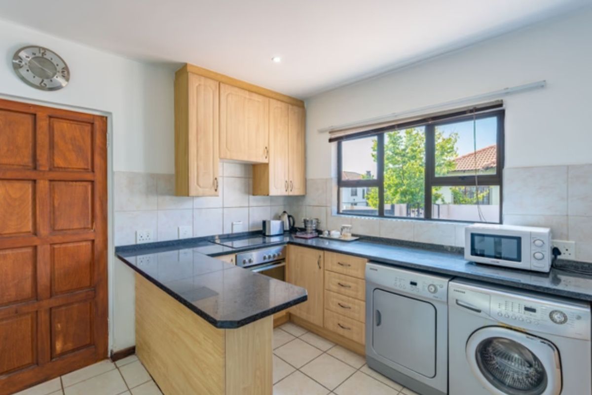 A functional kitchen featuring light wood cabinetry, dark granite countertops, tiled backsplash, and integrated laundry appliance space.