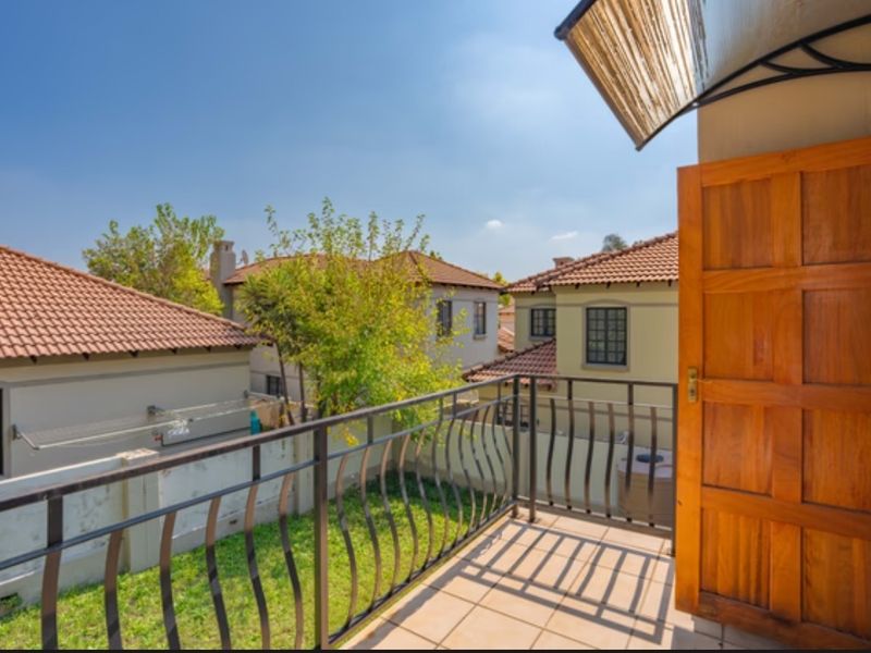 A private balcony featuring tiled flooring, a wrought iron railing, and a wooden door, overlooking the surrounding residential neighborhood.