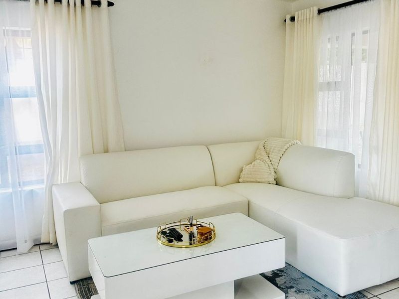 A bright living room featuring neutral tiled flooring, recessed ceiling lighting, and dual windows dressed with curtain rods.