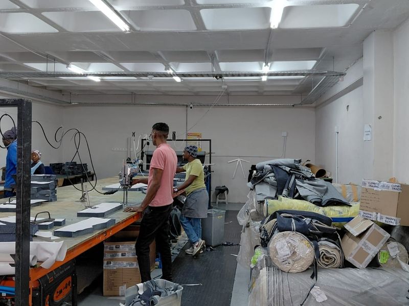 Industrial workspace featuring concrete flooring, overhead fluorescent lighting, and fixed workbenches suitable for manufacturing or production operations.
