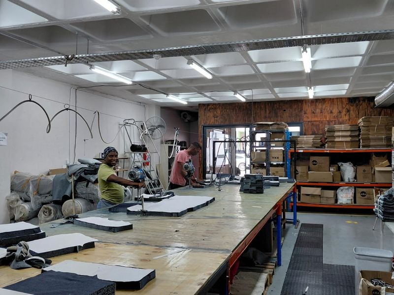 Industrial workspace featuring a waffle slab ceiling, fluorescent lighting, extensive metal shelving for storage, and a large central workbench for manufacturing operations.