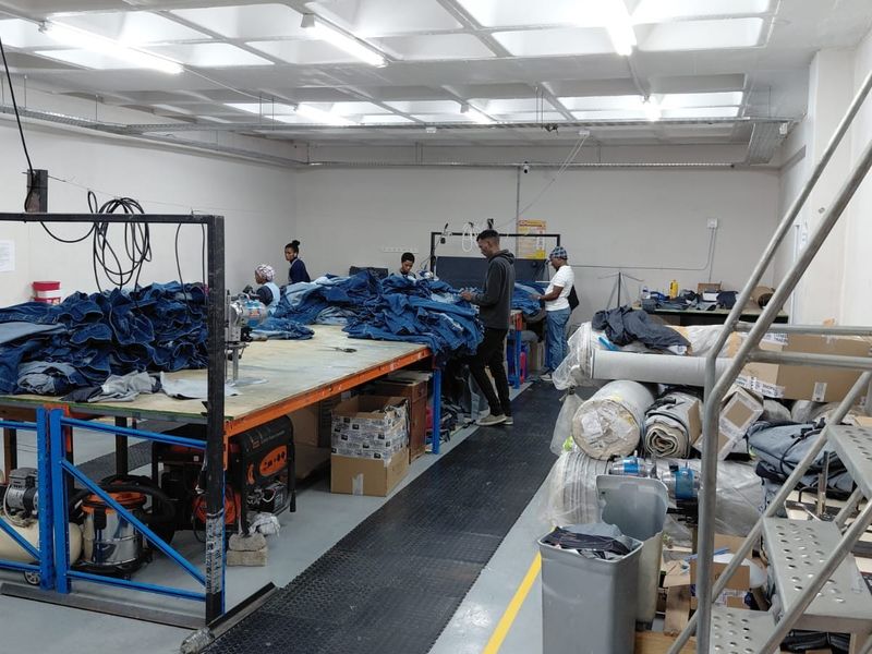 Industrial workspace featuring high ceilings with fluorescent lighting, durable epoxy flooring, and exposed electrical conduit, suitable for manufacturing or production operations.