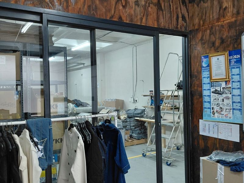 Industrial utility space featuring a sliding glass partition, plywood wall paneling, and concrete flooring, currently utilized for storage and operational workspace.