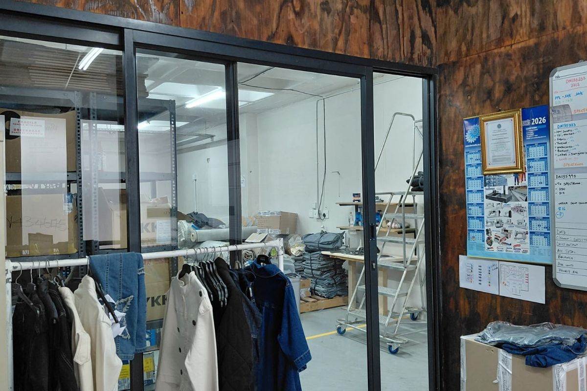 Industrial utility space featuring a sliding glass partition, plywood wall paneling, and concrete flooring, currently utilized for storage and operational workspace.