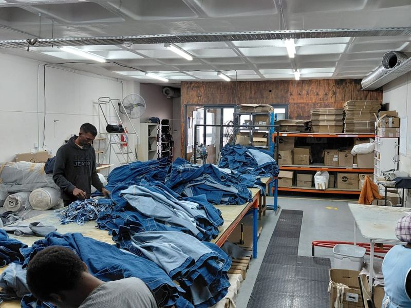 Industrial workspace featuring exposed ceiling ducting, cable trays, fluorescent lighting, and heavy-duty shelving units suitable for manufacturing or storage operations.