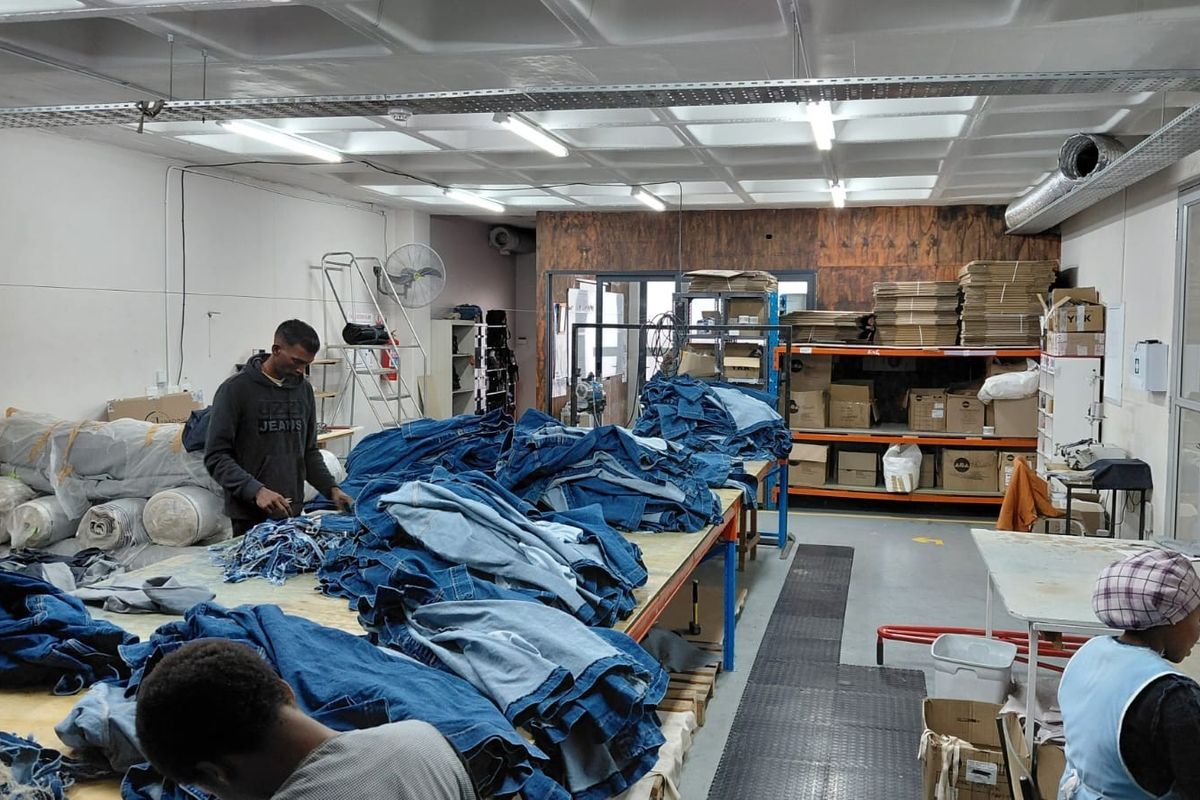 Industrial workspace featuring exposed ceiling ducting, cable trays, fluorescent lighting, and heavy-duty shelving units suitable for manufacturing or storage operations.