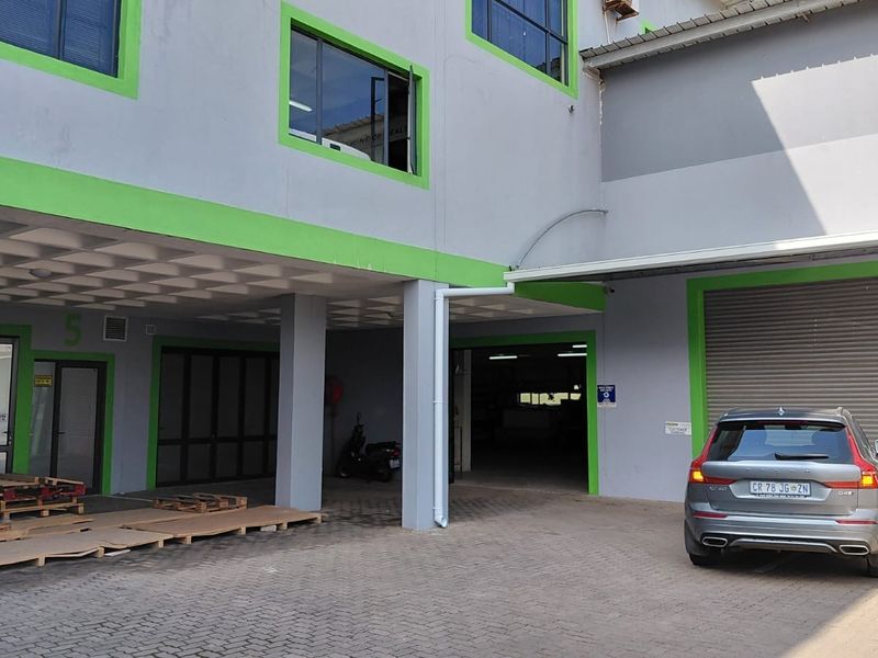 Industrial property exterior featuring a paved driveway, roller shutter door, and covered entrance area with concrete columns.