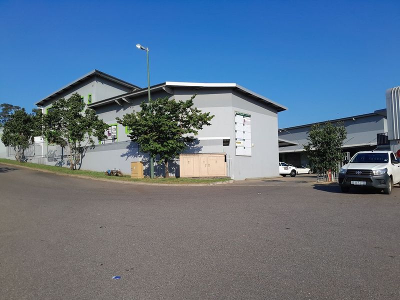 Exterior view of an industrial property featuring a paved driveway, perimeter wall, and signage board, showing the main entrance area.