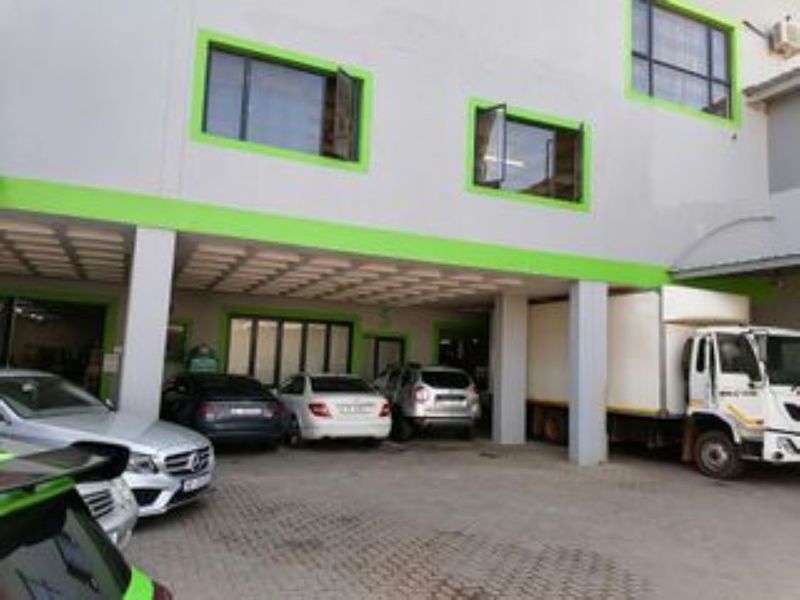 Front exterior view of an industrial building featuring a covered parking area, paved driveway, and multi-level facade with green-trimmed window frames.