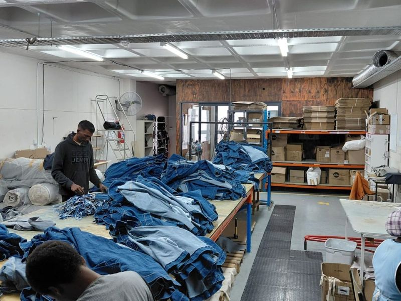 Industrial workspace featuring exposed ceiling grid, overhead cable management, and heavy-duty shelving units suitable for manufacturing or storage operations.