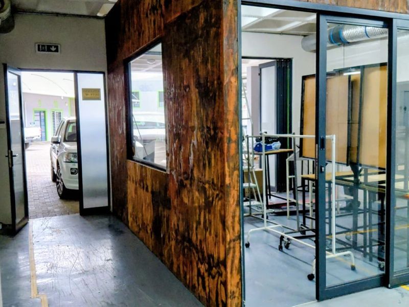 Industrial office space featuring a glass partition, exposed ceiling ducting, and plywood wall paneling, providing a functional and modern workspace environment.