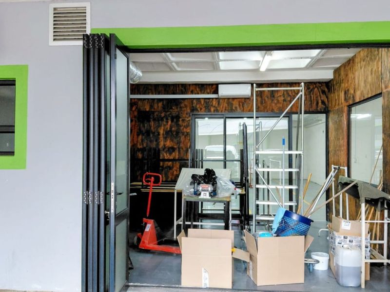 Industrial utility space featuring bi-fold doors, epoxy flooring, and integrated air conditioning, suitable for storage or workshop use.