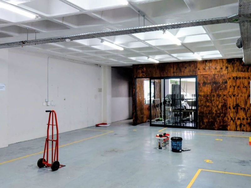 Spacious industrial utility area featuring a waffle slab ceiling, exposed cable management, epoxy flooring, and a glass-partitioned office or storage section.
