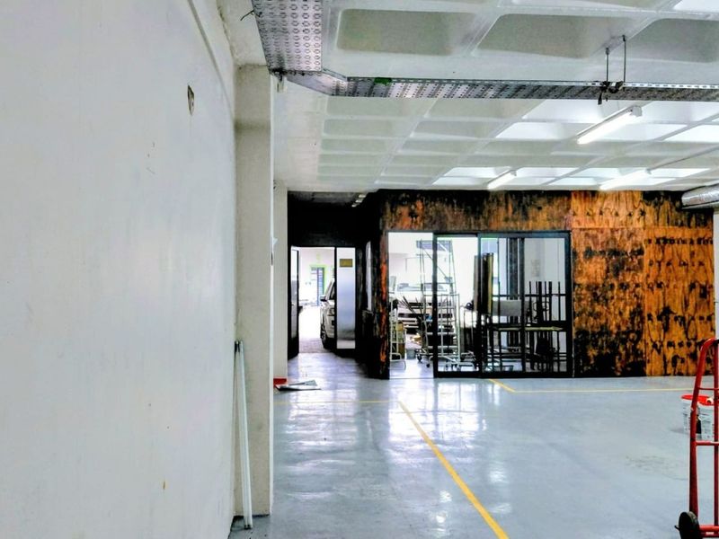 Spacious industrial utility area featuring durable epoxy flooring, exposed waffle slab ceiling, and a glass-partitioned office or storage section.