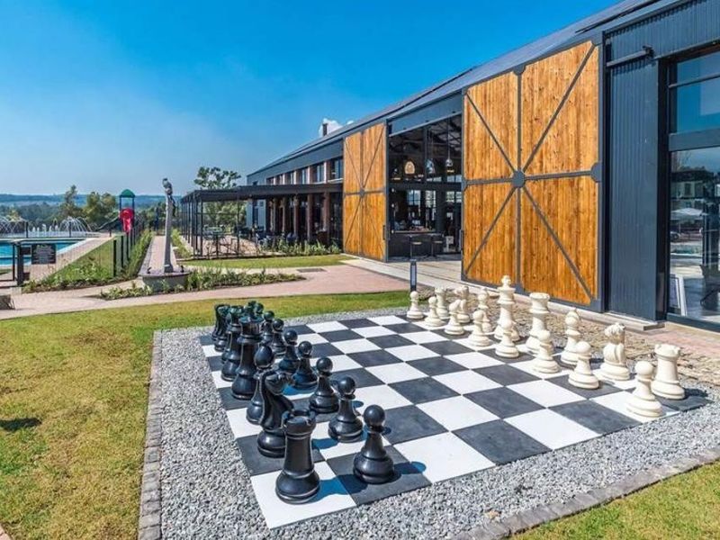 A modern clubhouse facility featuring large sliding barn-style doors, expansive glass windows, and an adjacent swimming pool area with landscaped grounds.