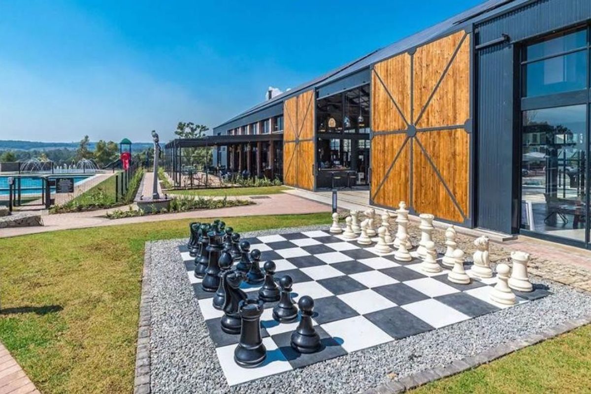 A modern clubhouse facility featuring large sliding barn-style doors, expansive glass windows, and an adjacent swimming pool area with landscaped grounds.