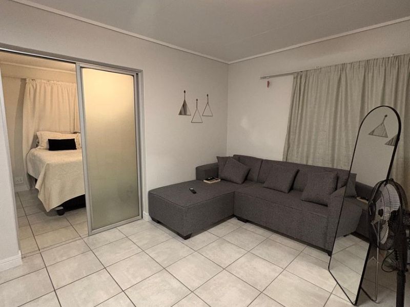 Open plan living area featuring neutral tiled flooring and a sliding glass door leading to an adjacent bedroom space.