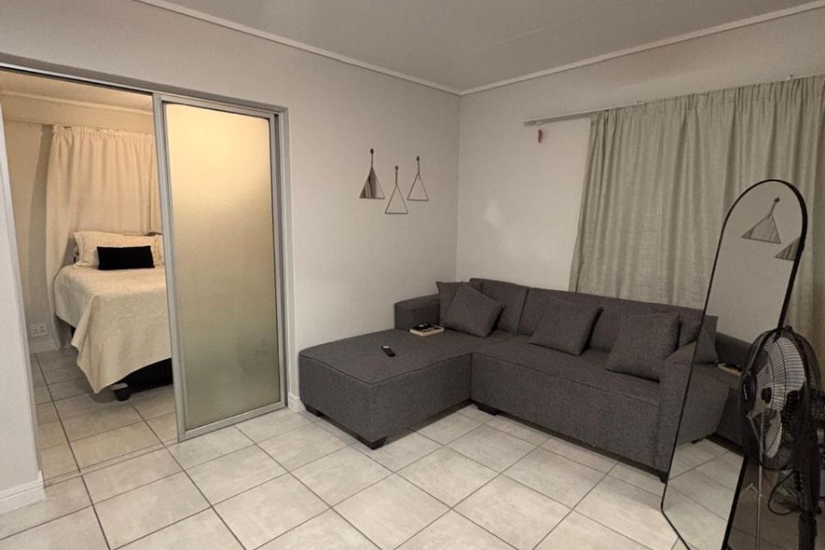 Open plan living area featuring neutral tiled flooring and a sliding glass door leading to an adjacent bedroom space.
