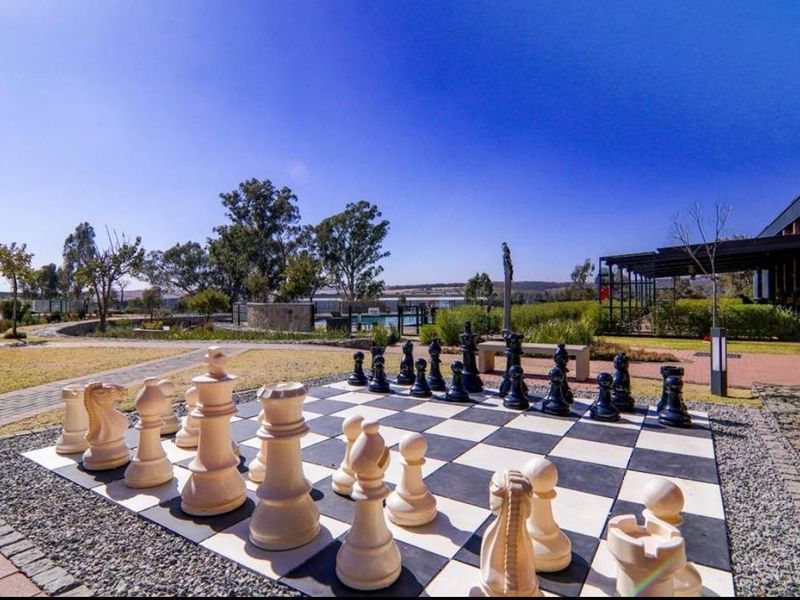 A well-maintained outdoor garden area featuring a large, permanent outdoor chess set, paved pathways, and landscaped surroundings within the apartment complex grounds.