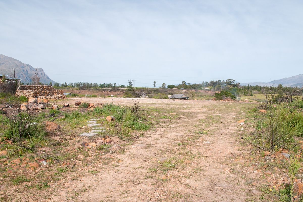 A wide-angle view of a vacant residential plot featuring natural terrain, stone wall remnants, and scenic mountain views in the background.