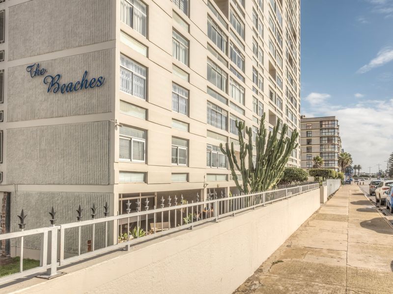 Exterior view of The Beaches apartment building, featuring a multi-story facade with large windows and a secure perimeter boundary wall.