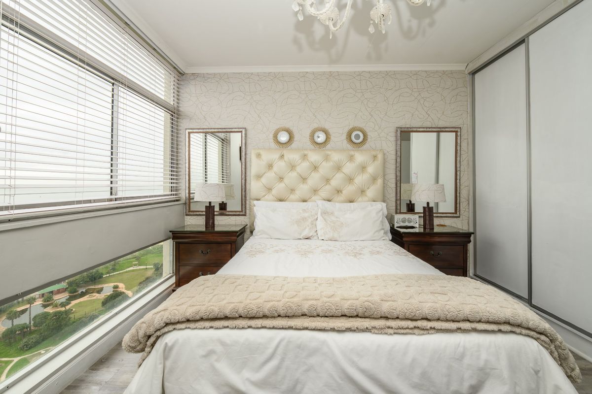 A well-maintained bedroom featuring a built-in sliding wardrobe, patterned wallpaper, and large windows offering scenic views.