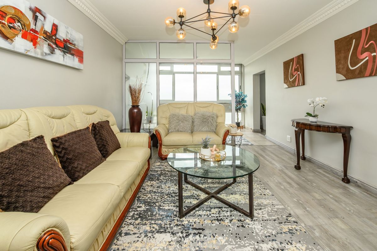 A well-maintained living room featuring laminate flooring, crown molding, and a modern chandelier, with a glass partition leading to an adjacent space.