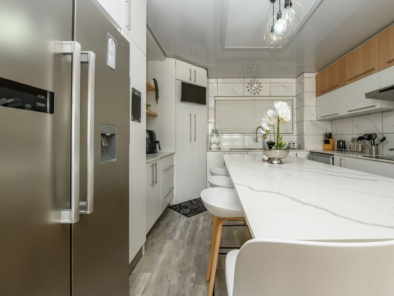Modern kitchen featuring a large marble-look quartz island, sleek white and wood-tone cabinetry, stainless steel extractor fan, and high-quality laminate flooring.