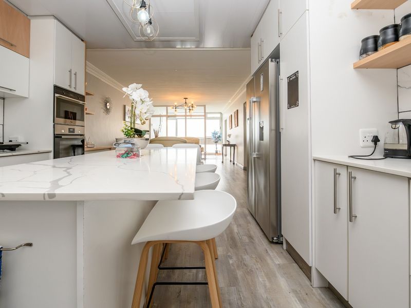 Modern open-plan kitchen featuring a stone island, built-in appliances, and sleek cabinetry, flowing seamlessly into the living area.