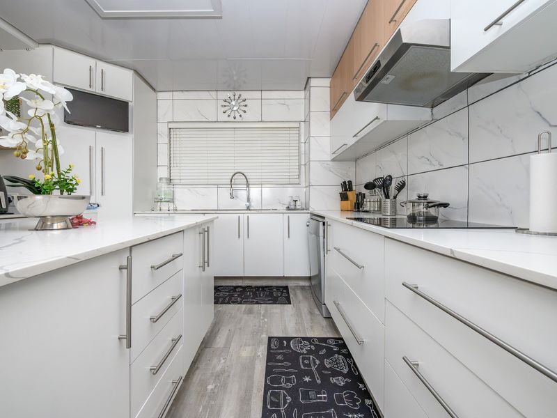 Modern, well-maintained kitchen featuring white cabinetry, marble-look countertops, integrated appliances, and a sleek tiled backsplash with contemporary finishes.