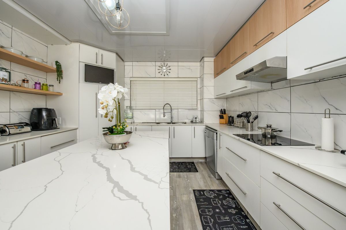 Modern kitchen featuring a large quartz-topped island, sleek white and wood-tone cabinetry, integrated appliances, and stylish marble-effect wall tiling.