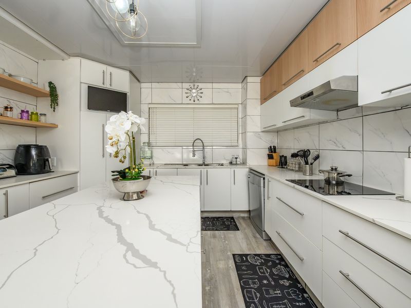Modern kitchen featuring a large quartz-topped island, sleek white and wood-tone cabinetry, integrated appliances, and stylish marble-effect wall tiling.