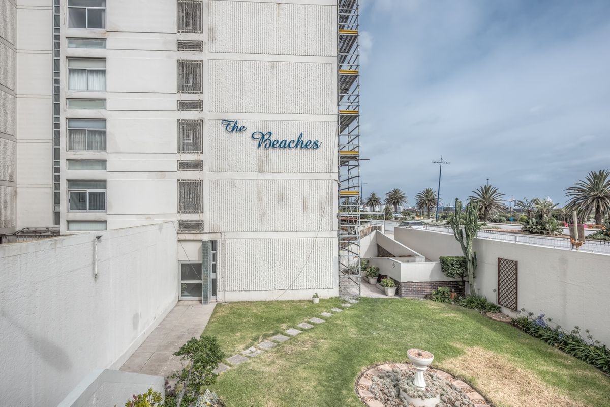 Exterior view of The Beaches apartment complex featuring a landscaped garden area and building facade currently undergoing maintenance with scaffolding.