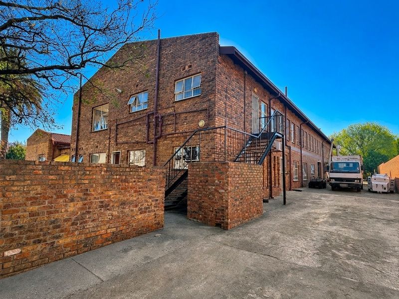 Rear view of a multi-story commercial brick building featuring an external metal staircase, concrete yard area, and perimeter brick walling.