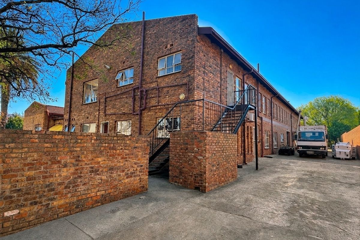 Rear view of a multi-story commercial brick building featuring an external metal staircase, concrete yard area, and perimeter brick walling.