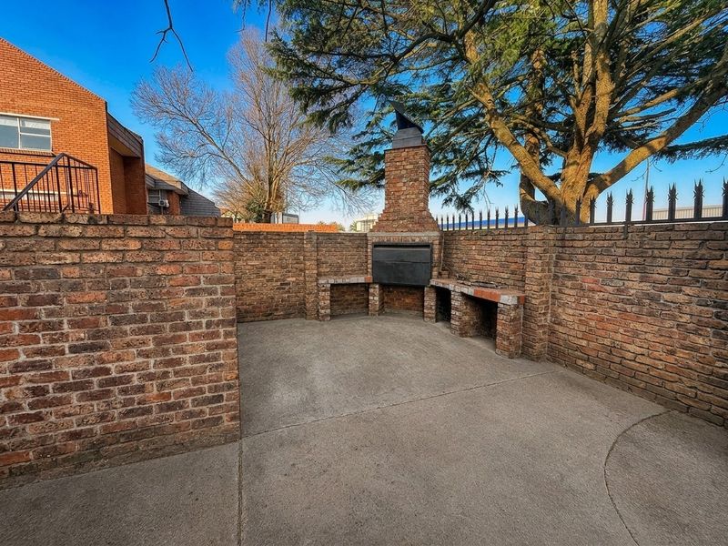 An outdoor patio area featuring a built-in brick braai, enclosed by brick walls and topped with security spikes.