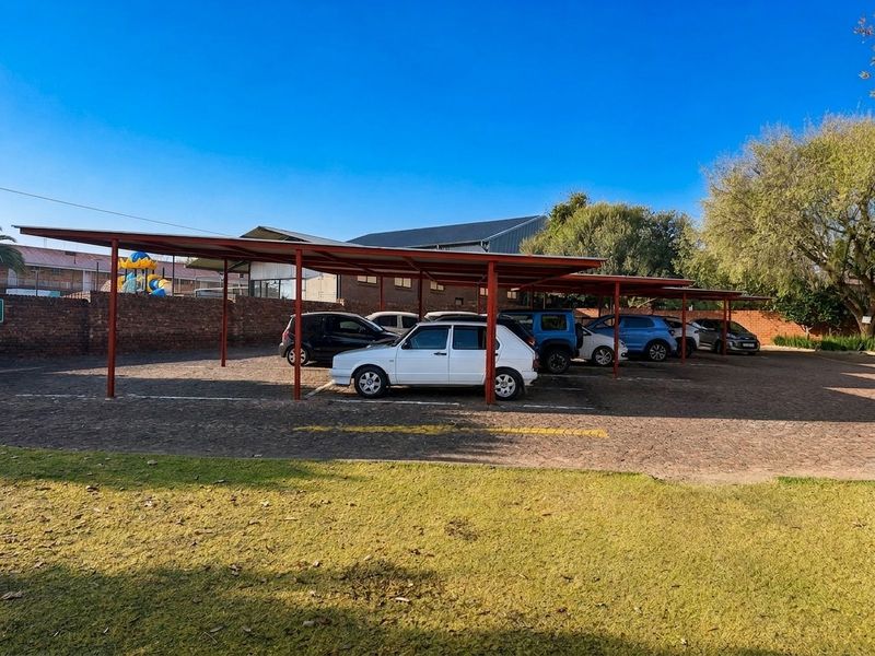 A commercial property featuring a paved parking area with multiple covered steel carport bays and a secure brick boundary wall.